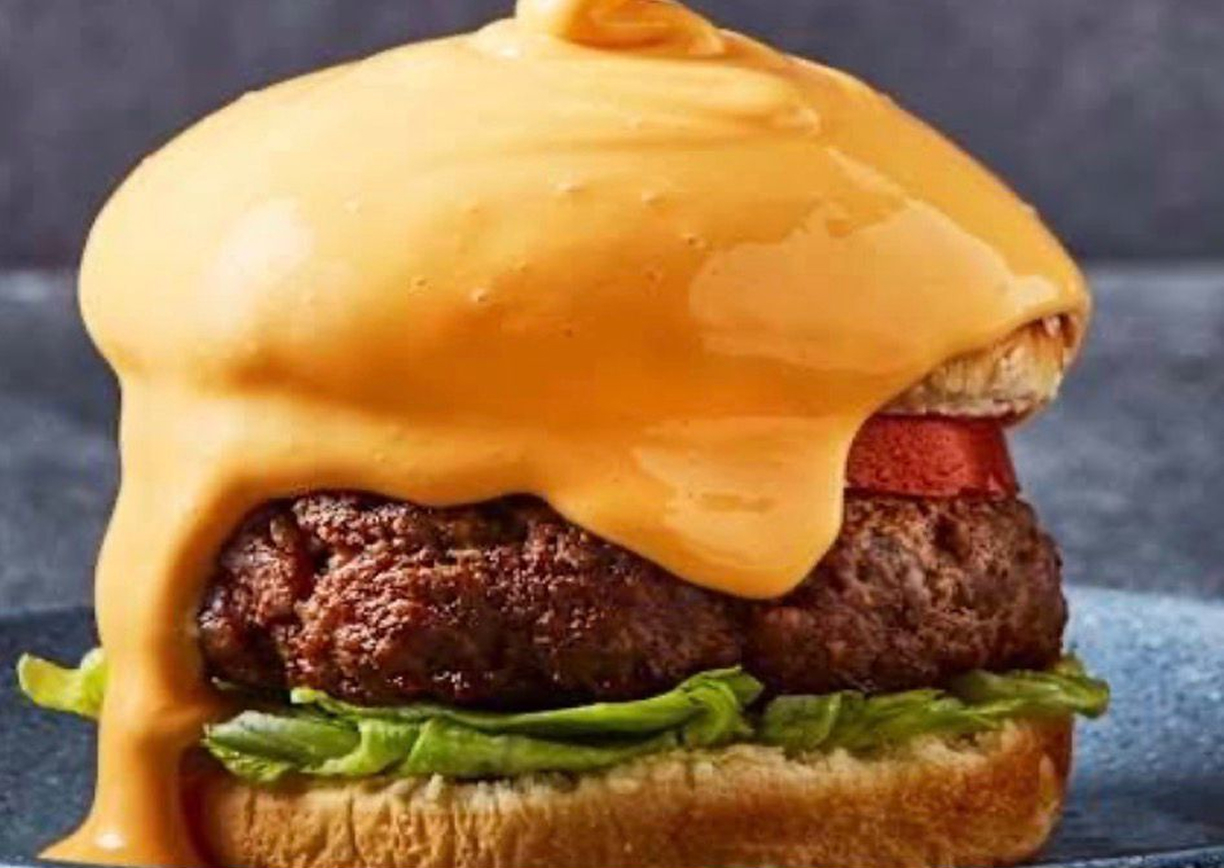 Volcán Chees Burguer de Caracas Burgers — Carne de res, lechuga, cebolla caramelizada, papas rayadas naturales, bañada en queso cheddar o mozzarella con trozos de tocino.